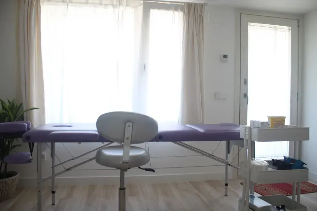 Una mesa de masajes con una silla en una habitación con ventana.