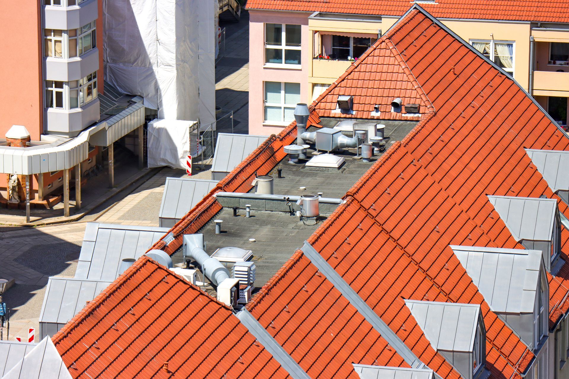 Toits recouverts de tuiles rouges et de conduits de ventilation argentés dans un quartier résidentiel urbain.