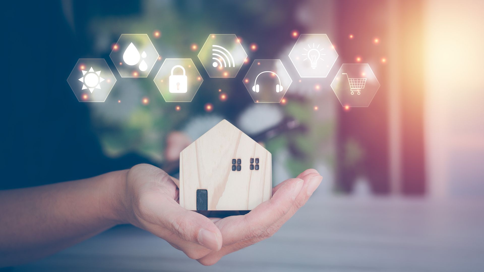 Main tenant une maquette de petite maison avec des icônes domotiques lumineuses en arrière-plan