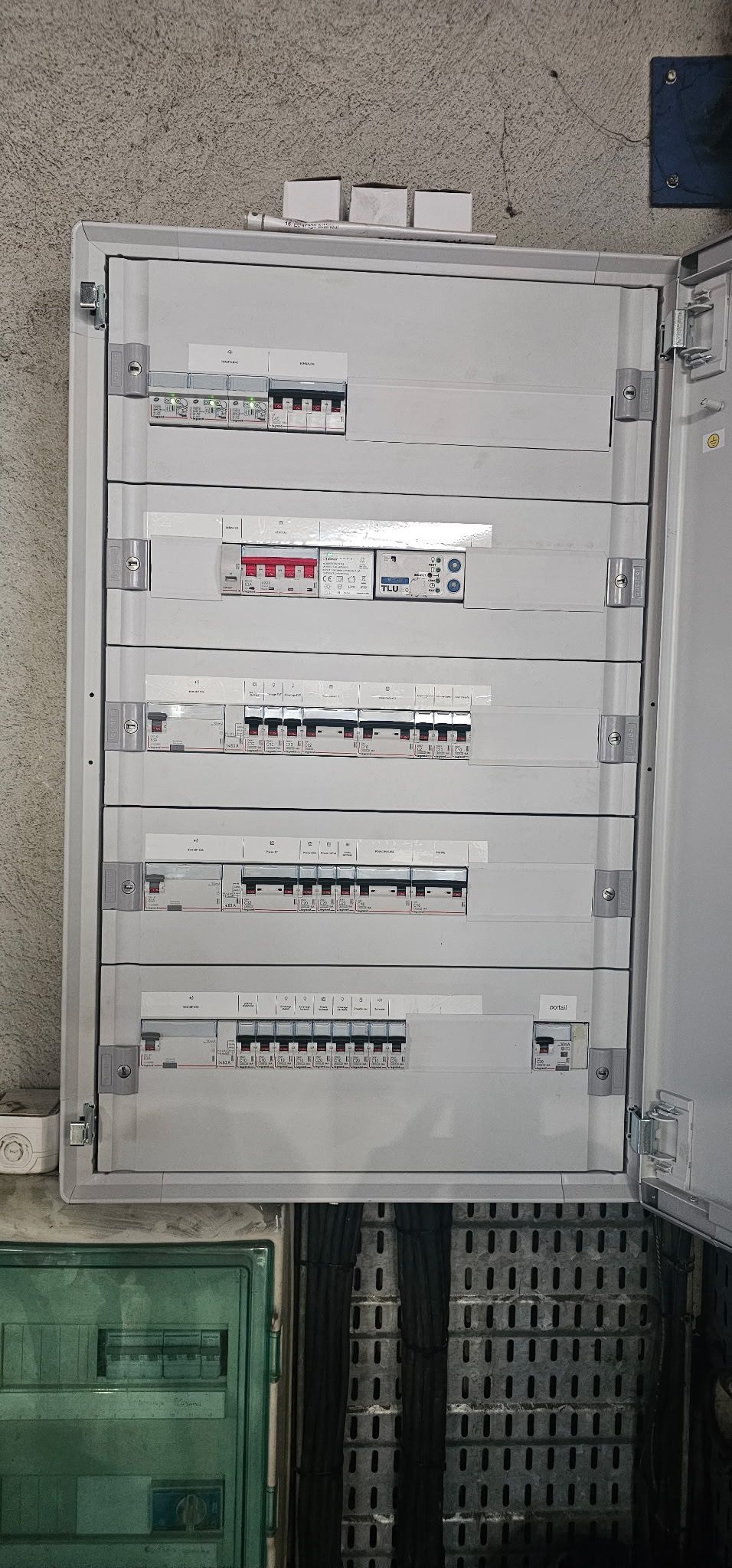 Panneau de commande électrique blanc avec interrupteurs étiquetés, fixé sur un mur en béton à l'extérieur.