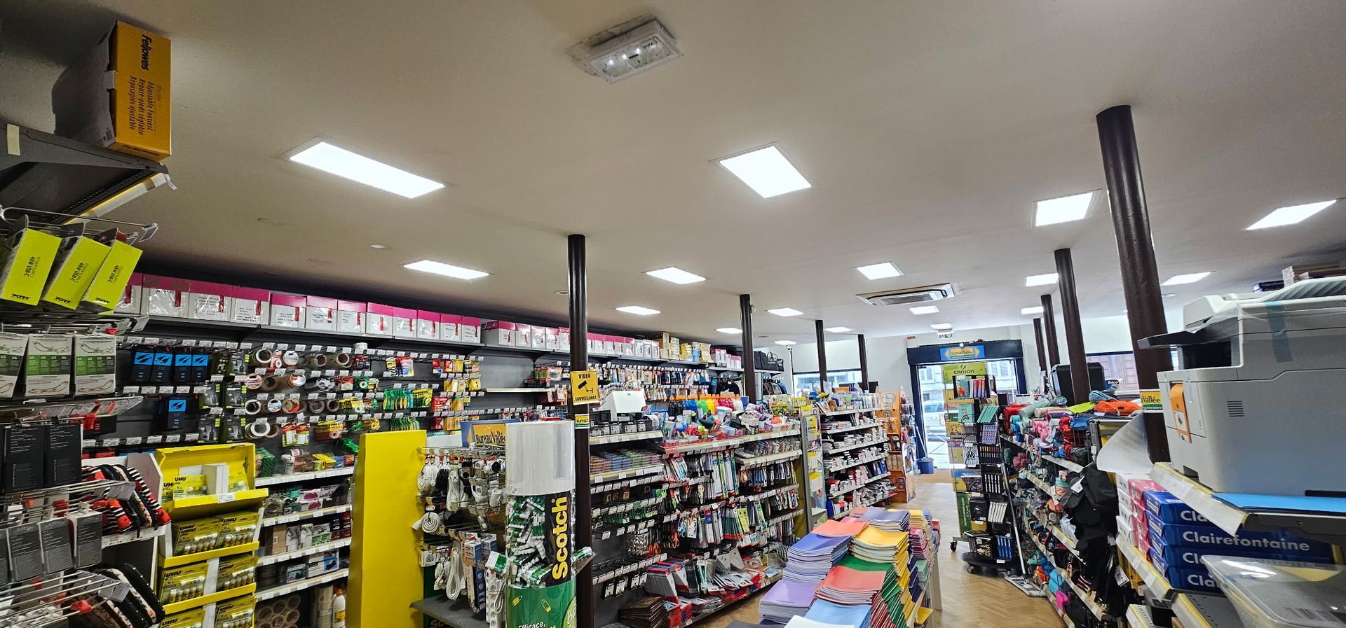 Allée d'un magasin bien éclairée, avec des étagères de produits emballés et des panneaux de solde jaunes.