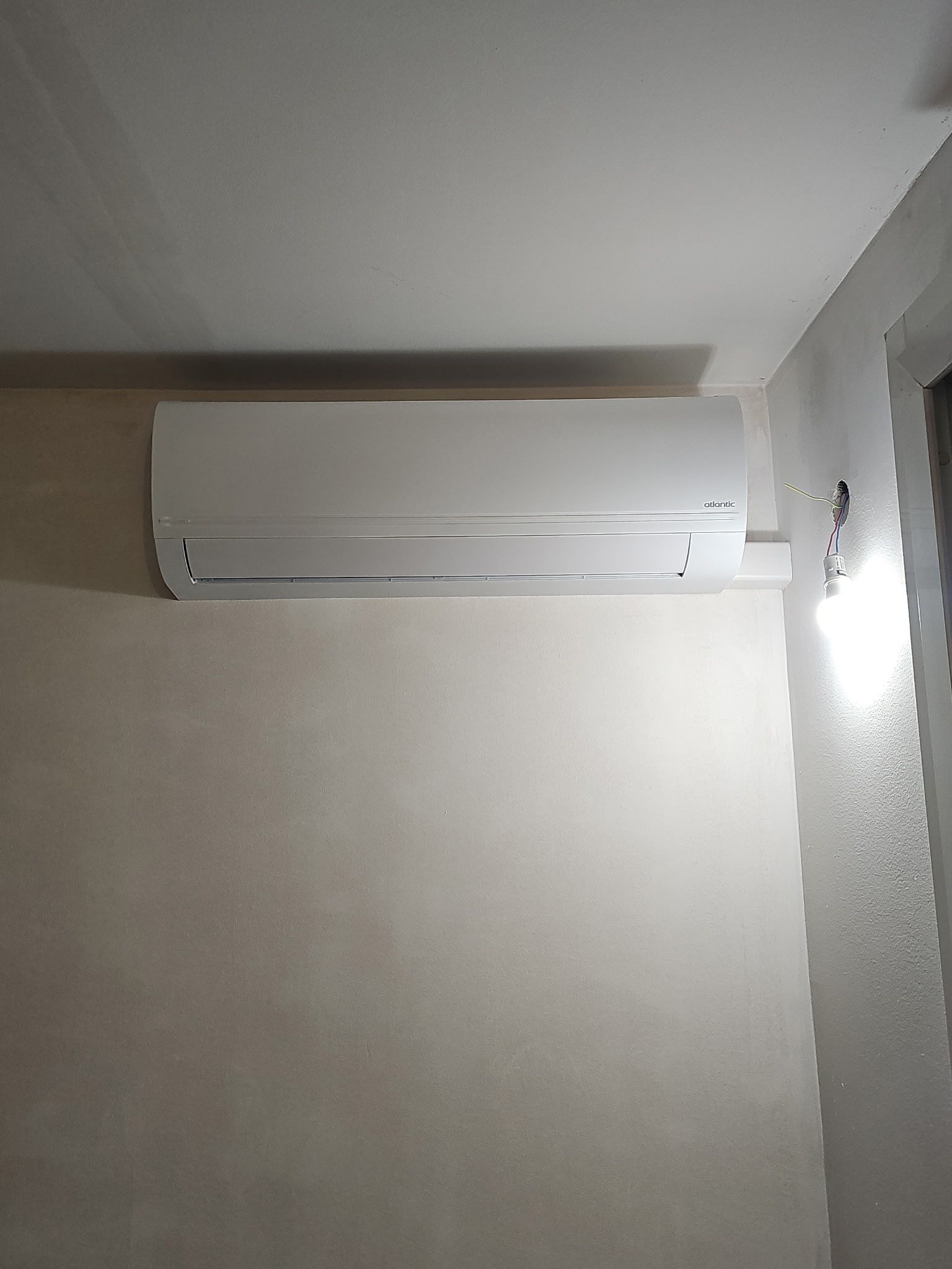 Climatiseur mural blanc près du plafond dans une pièce sobre.