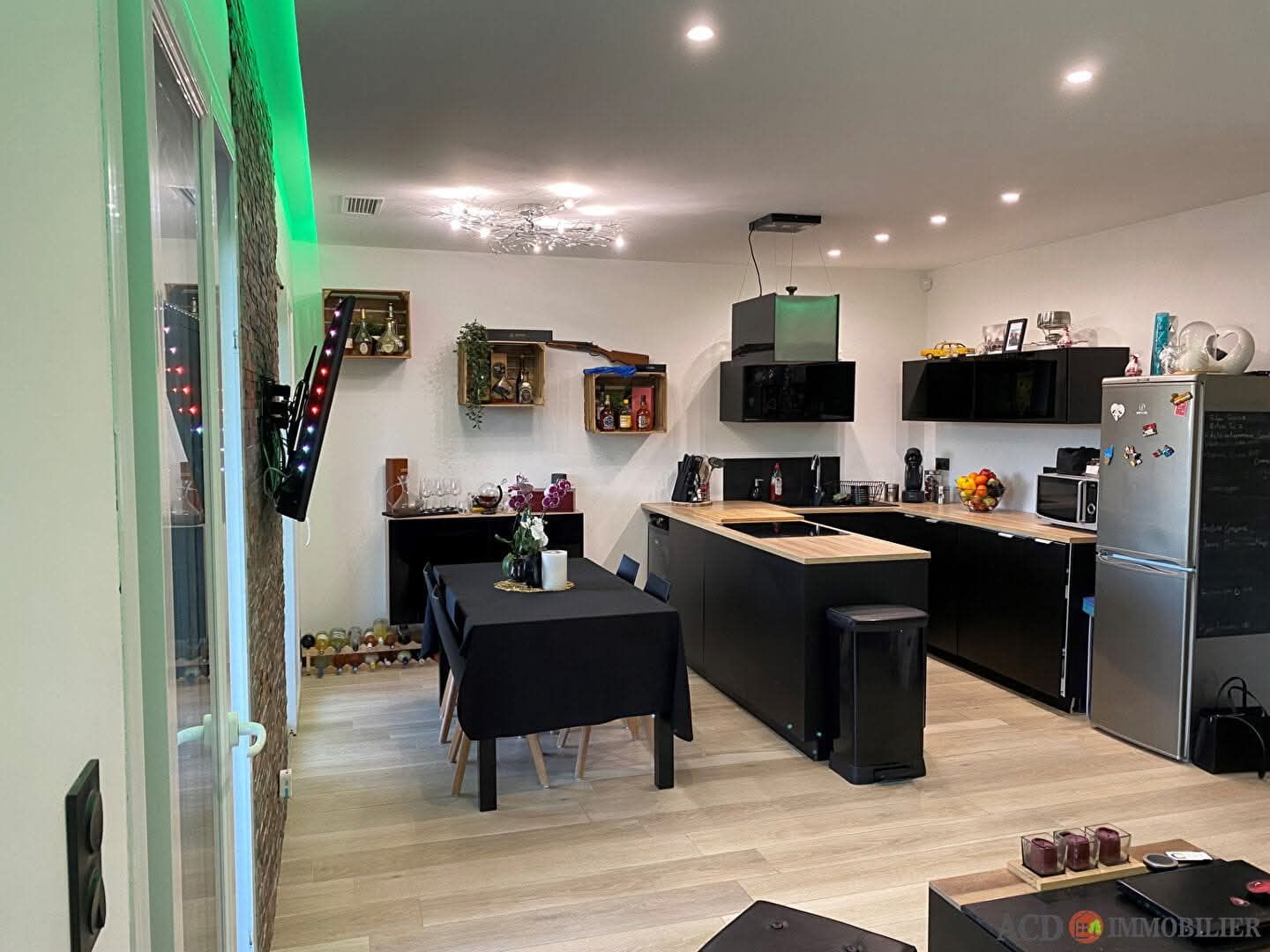 Cuisine et salle à manger ouvertes et modernes avec armoires noires, îlot en bois et réfrigérateur en acier inoxydable