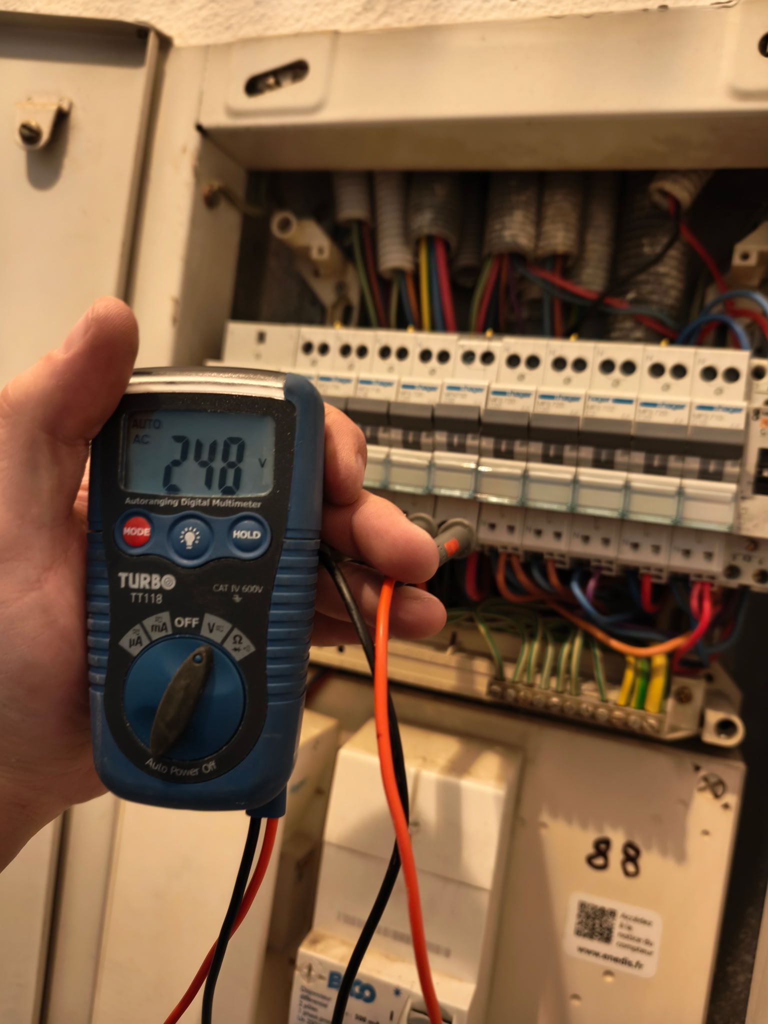 Main tenant un multimètre numérique mesurant le câblage à l'intérieur d'un tableau électrique.
