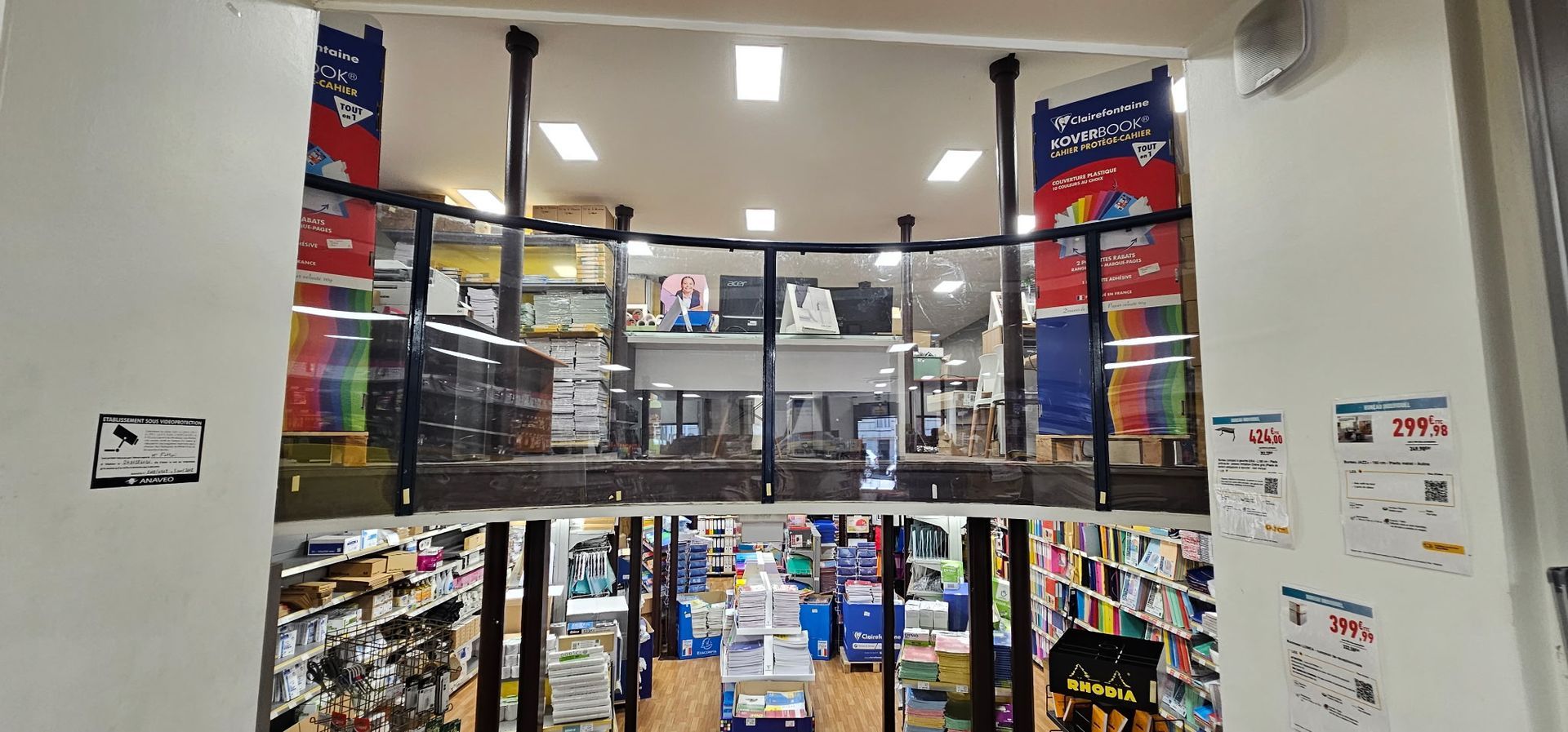 Entrée du magasin avec portes vitrées, étagères remplies de marchandises et banderoles rouges de soldes au-dessus.