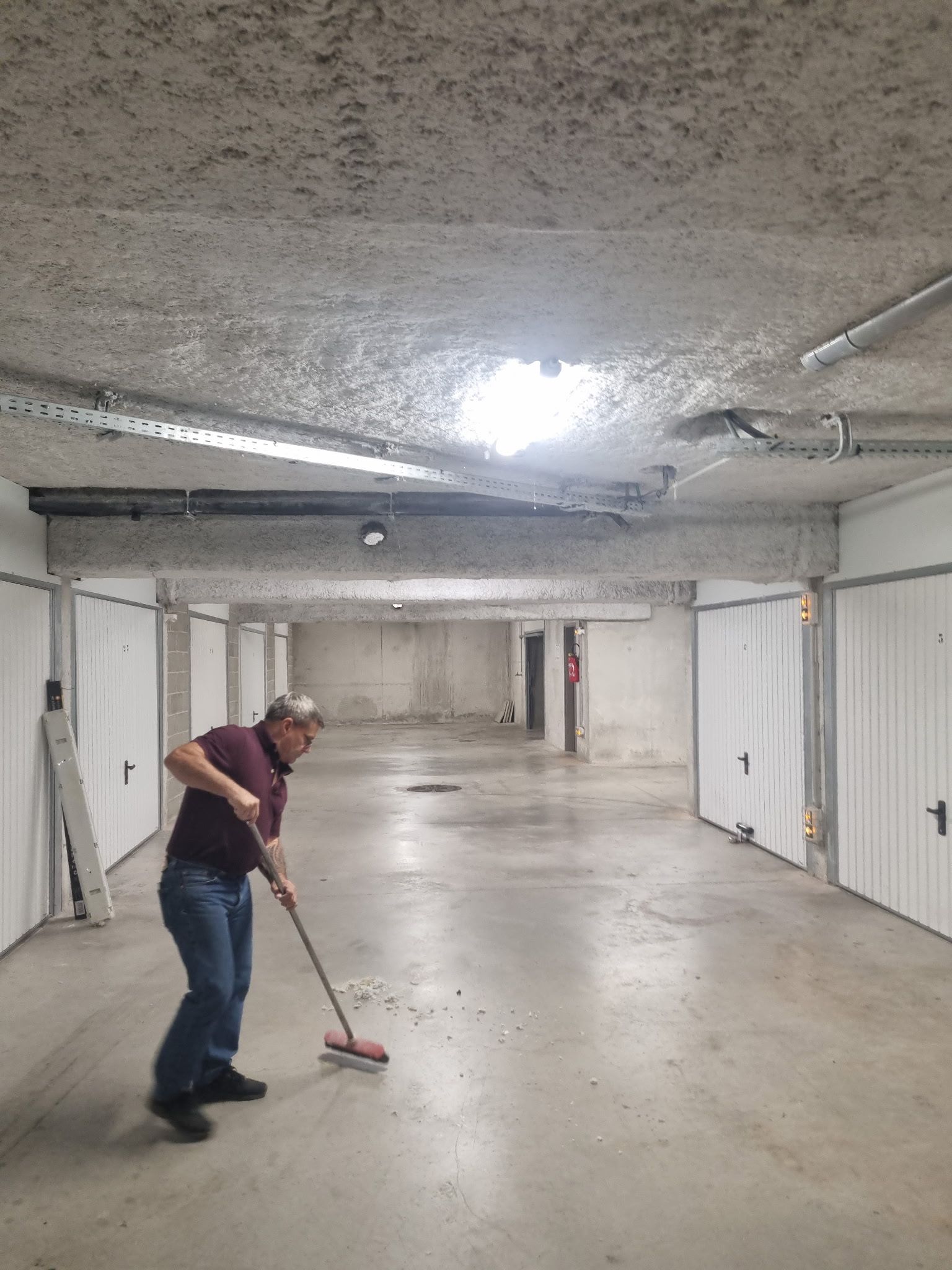 Un homme lave le sol en béton d'un garage souterrain faiblement éclairé.