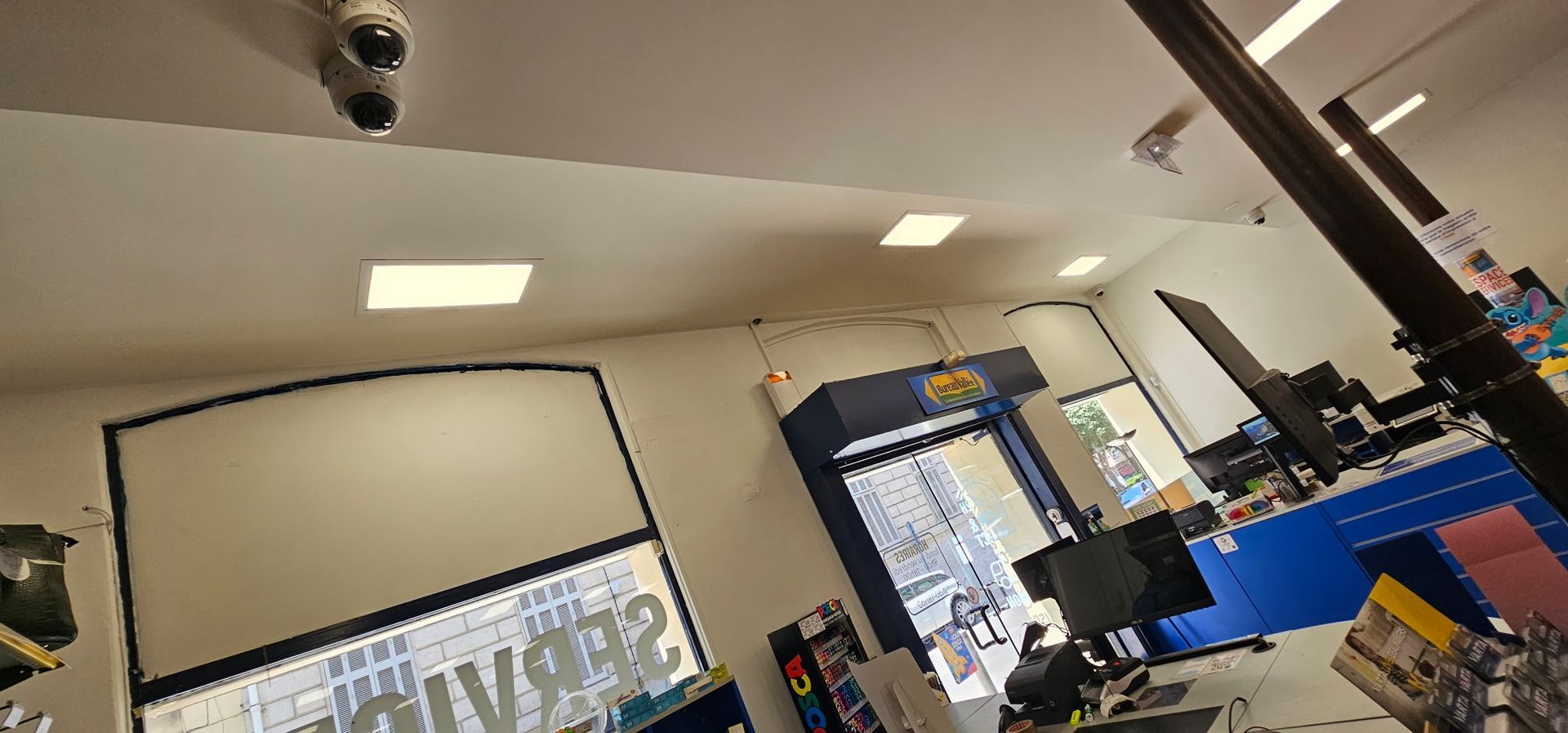 Vue inclinée de l'intérieur lumineux d'un magasin avec un écran de projection, des comptoirs bleus et des luminaires au plafond