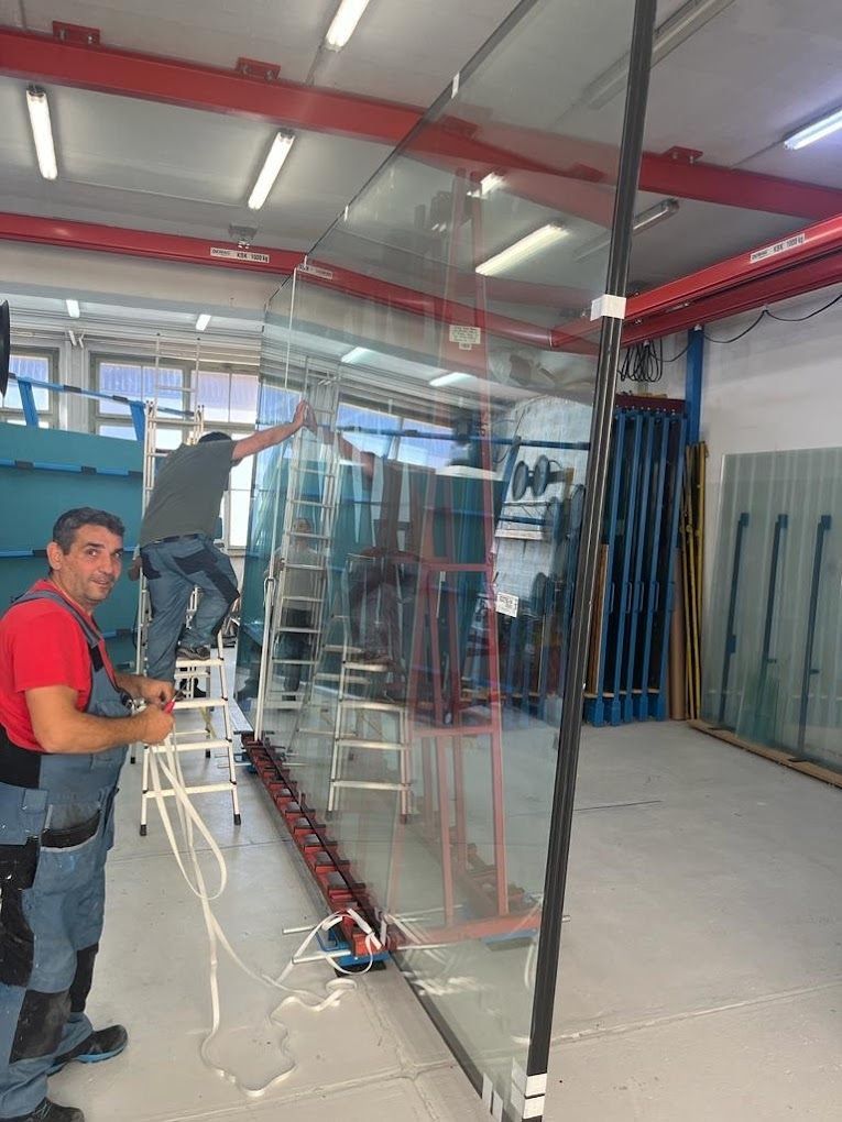 Deux hommes travaillent sur un grand morceau de verre dans une usine.