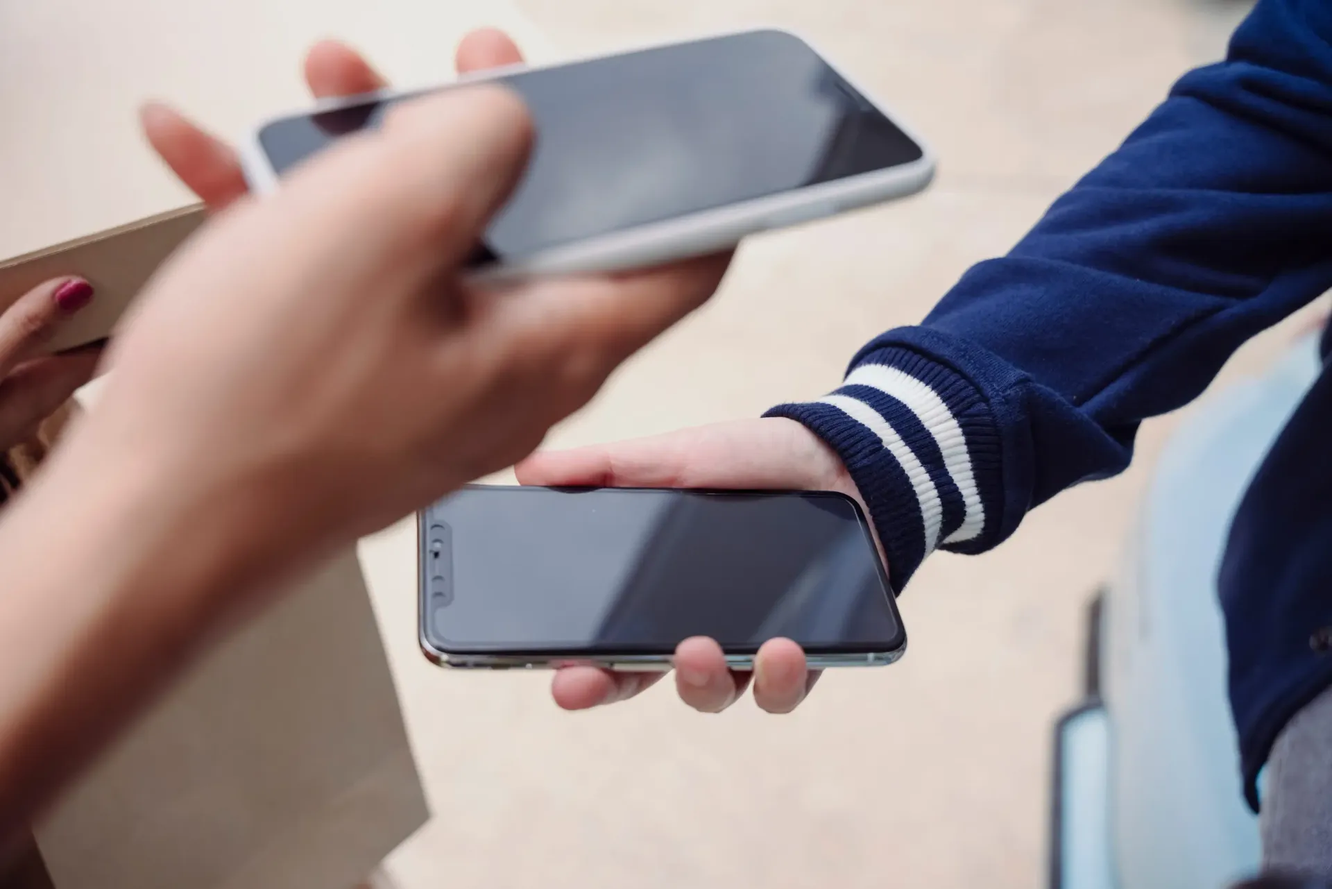 Primer plano de manos intercambiando teléfonos inteligentes; una persona con una chaqueta azul sostiene uno de los teléfonos.
