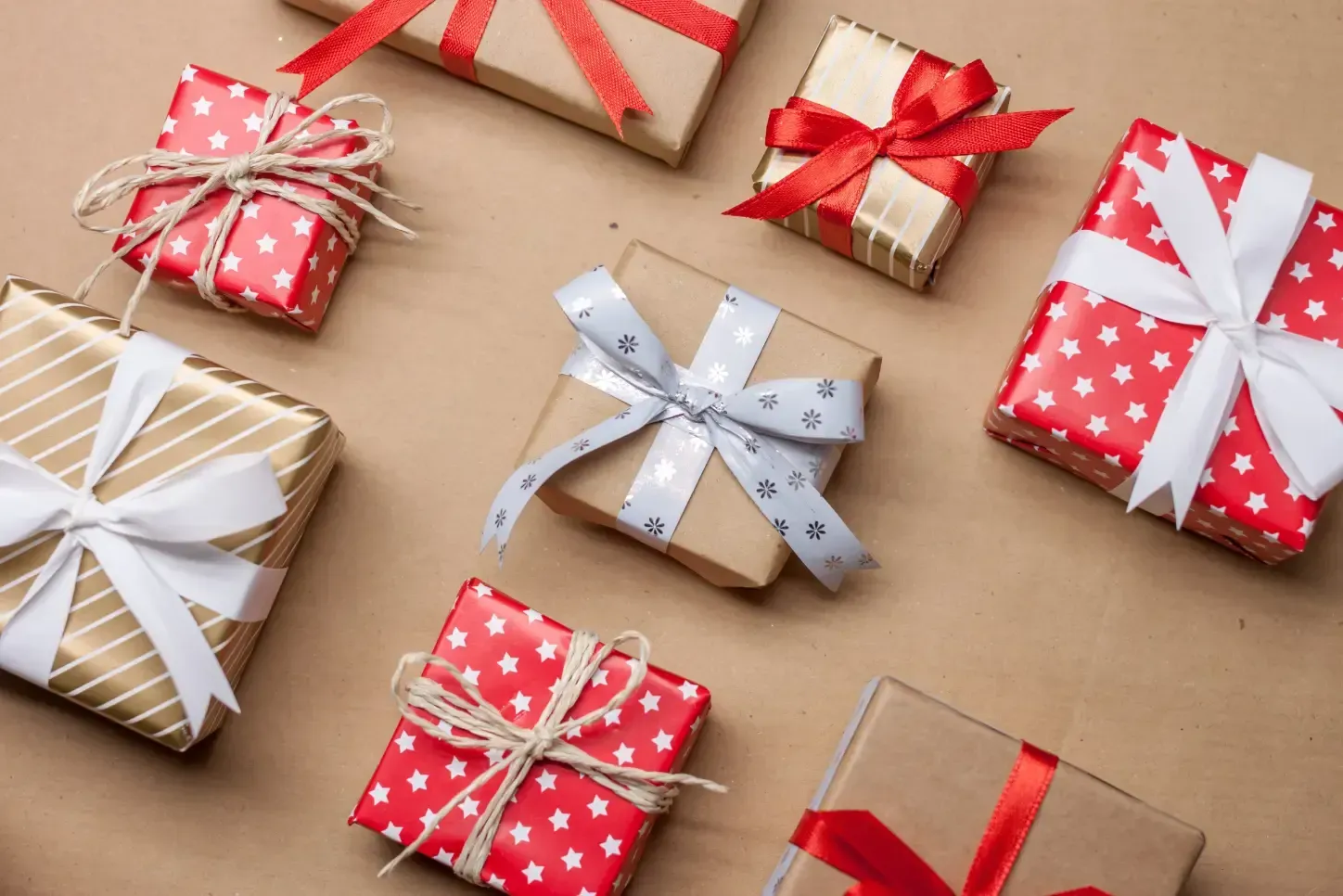 Cajas de regalo surtidas envueltas con cintas rojas, blancas y doradas sobre un fondo beige.