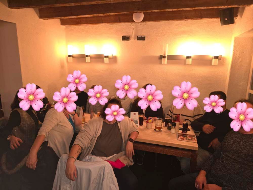 Eine Gruppe von Menschen sitzt um einen Tisch herum und hat rosa Blumen im Gesicht