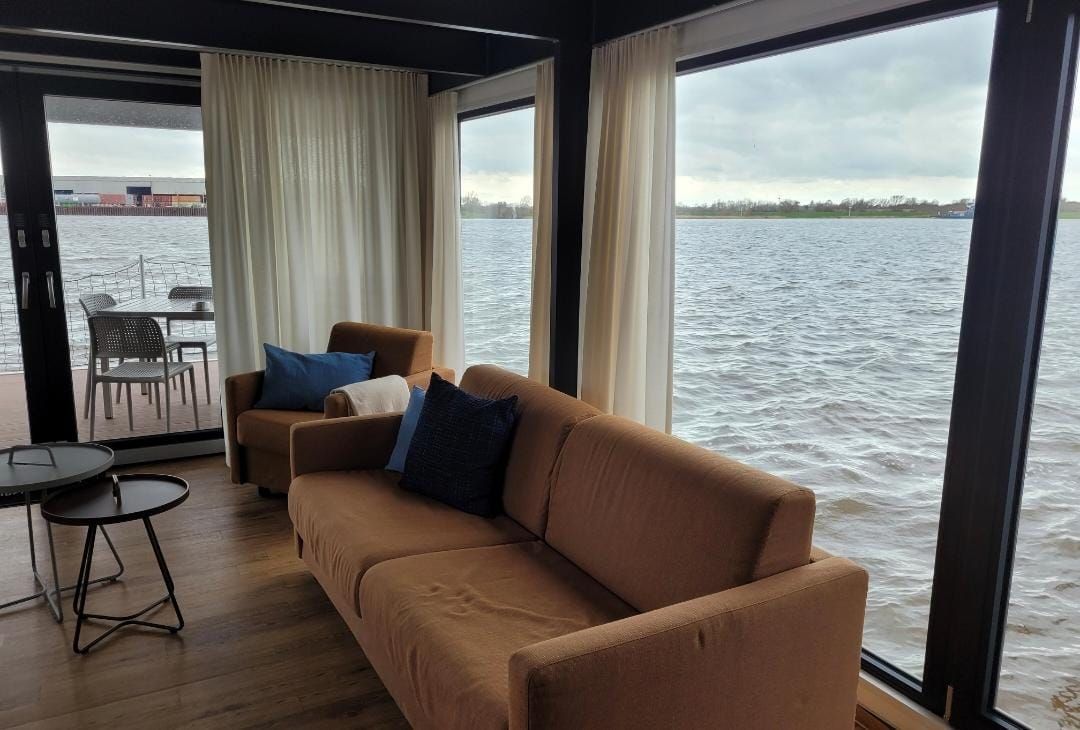 Ein Wohnzimmer mit Couch und Sessel und Blick aufs Wasser.