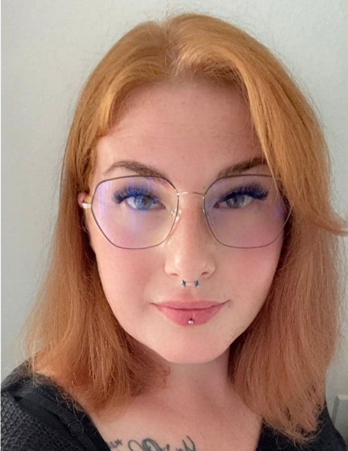 Eine Nahaufnahme einer Frau mit Brille und einer Tätowierung auf der Brust.