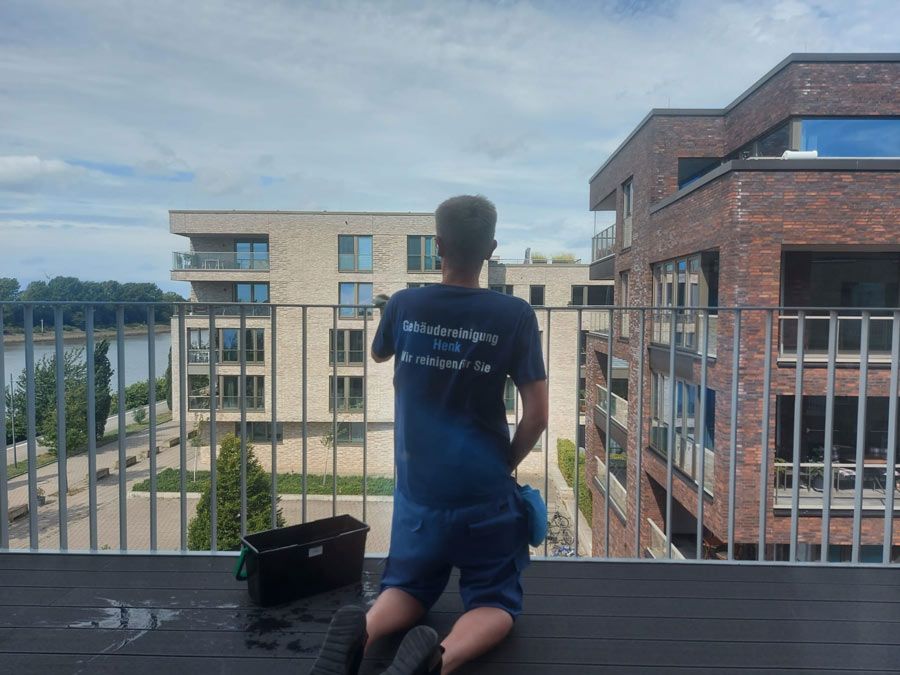 Ein Mann in einem blauen Hemd kniet auf einem Balkon mit Blick auf eine Stadt