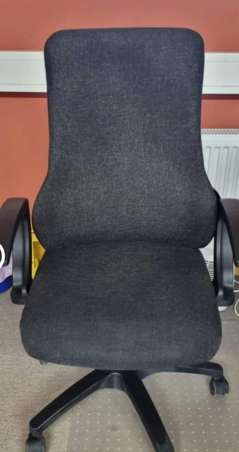 Schwarzer Bürostuhl mit Armlehnen vor einer roten Wand und einem weißen Heizkörper