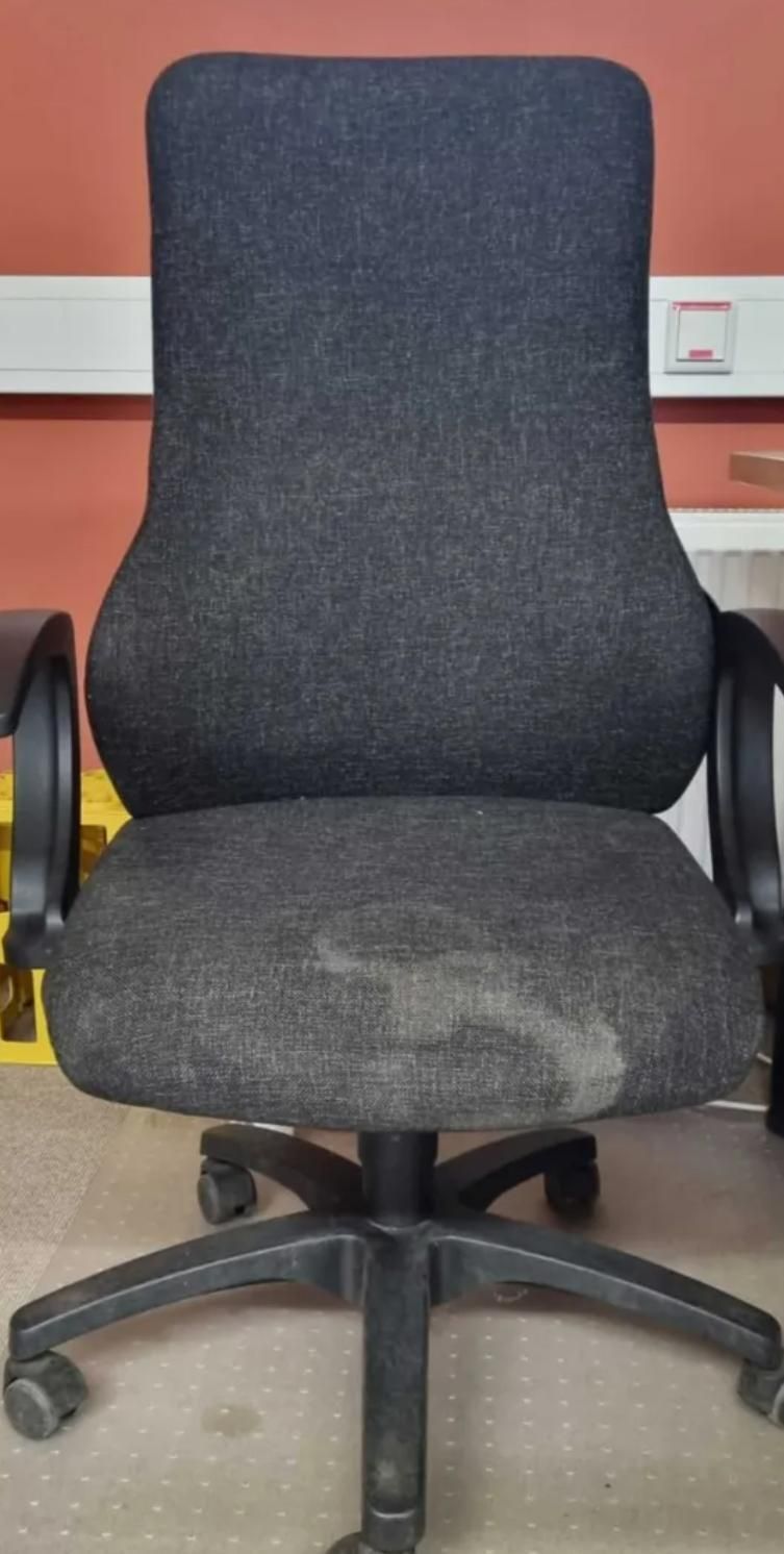Schwarzer Bürostuhl mit gepolsterter Sitzfläche und Rückenlehne auf Rollen in einem Raum mit roter Wand.