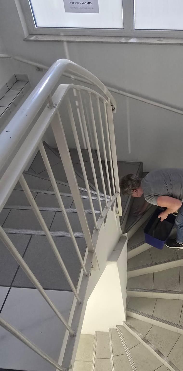 Person, die auf einem Treppenabsatz neben einem weißen Metallgeländer und gefliesten Stufen kauert