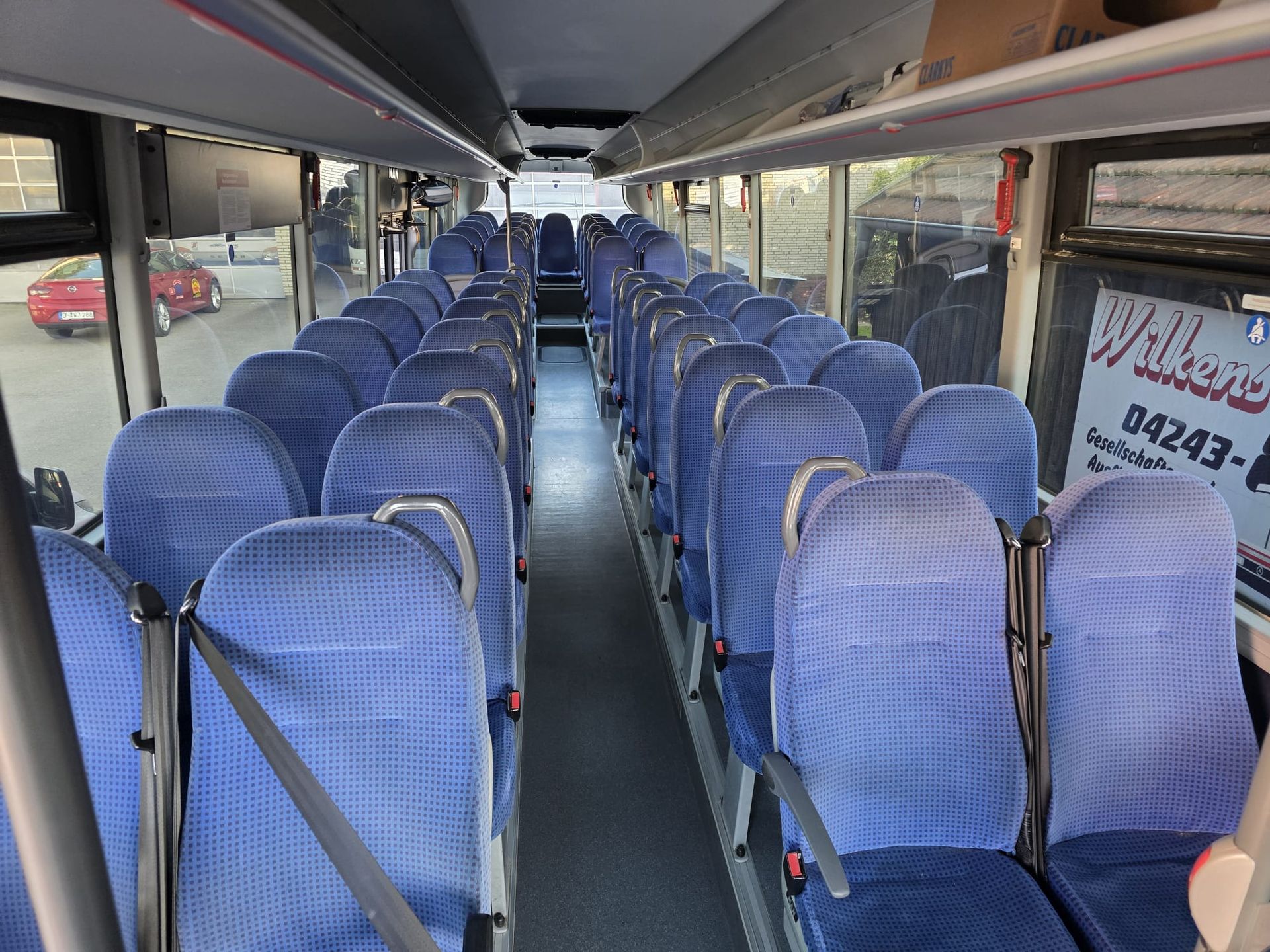 Leerer Innenraum eines Shuttle-Busses mit blauen Sitzen, Mittelgang und großen Fenstern
