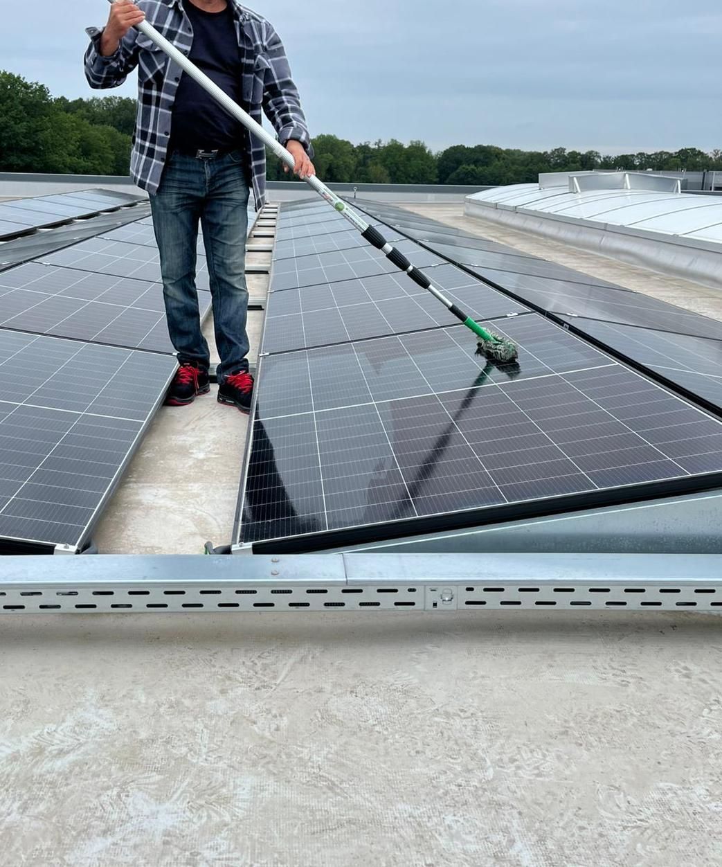 Person, die Solarmodule auf dem Dach mit einer langen Bürste reinigt