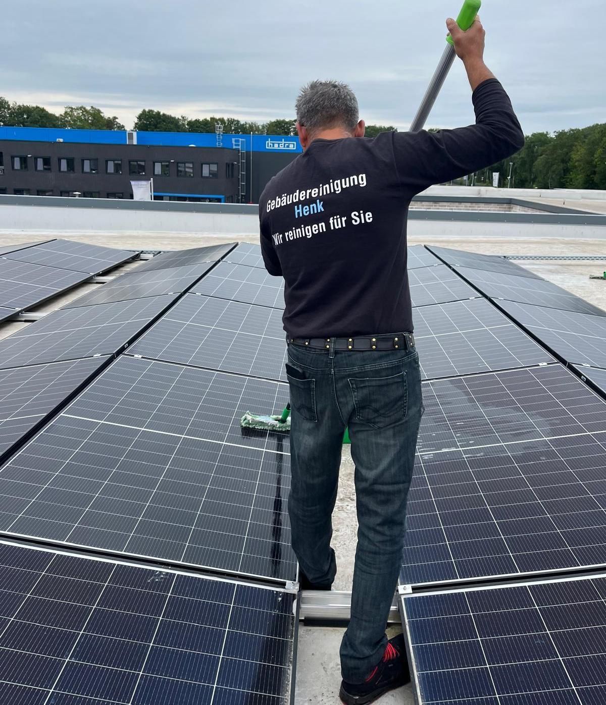 Ein Arbeiter inspiziert Solarmodule auf einem Dach und hält dabei ein grünes Werkzeug hoch.