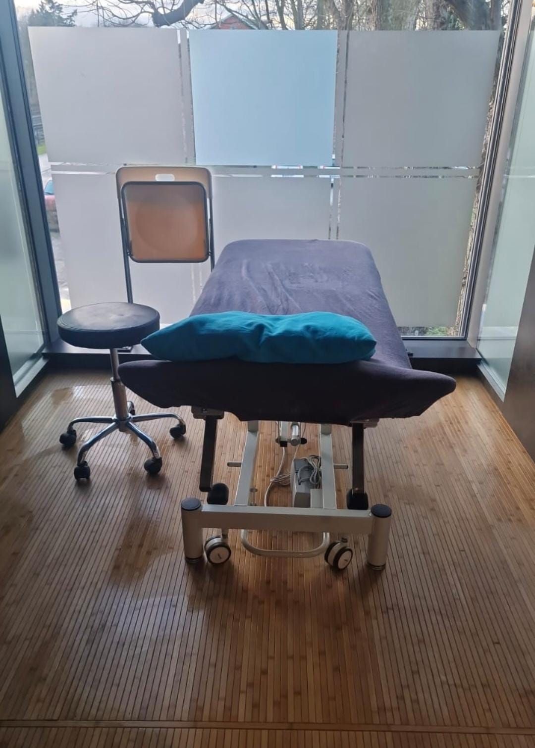 Eine Massageliege mit einem blauen Kissen darauf in einem Raum mit einem Stuhl.