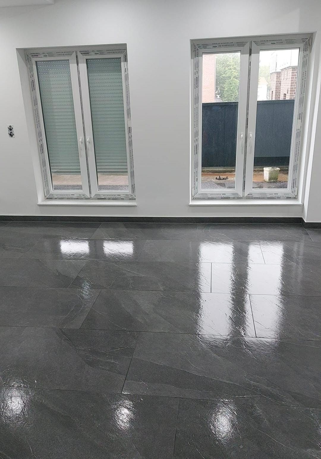 Ein Raum mit zwei Fenstern und einem schwarzen Fliesenboden.