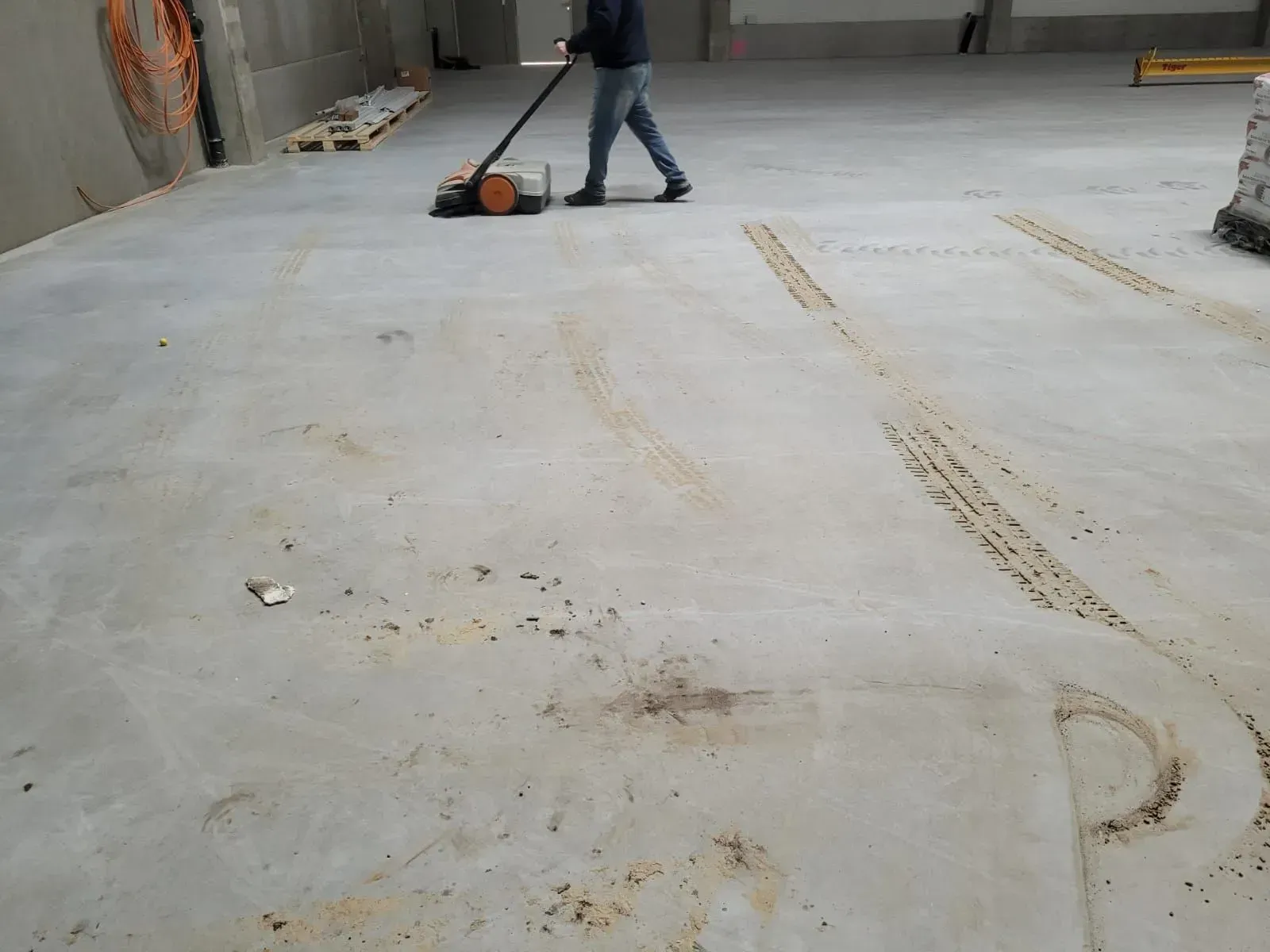 Person, der in einem unfertigen Industriebereich einen Bodenschleifer auf einer Betonplatte bedient