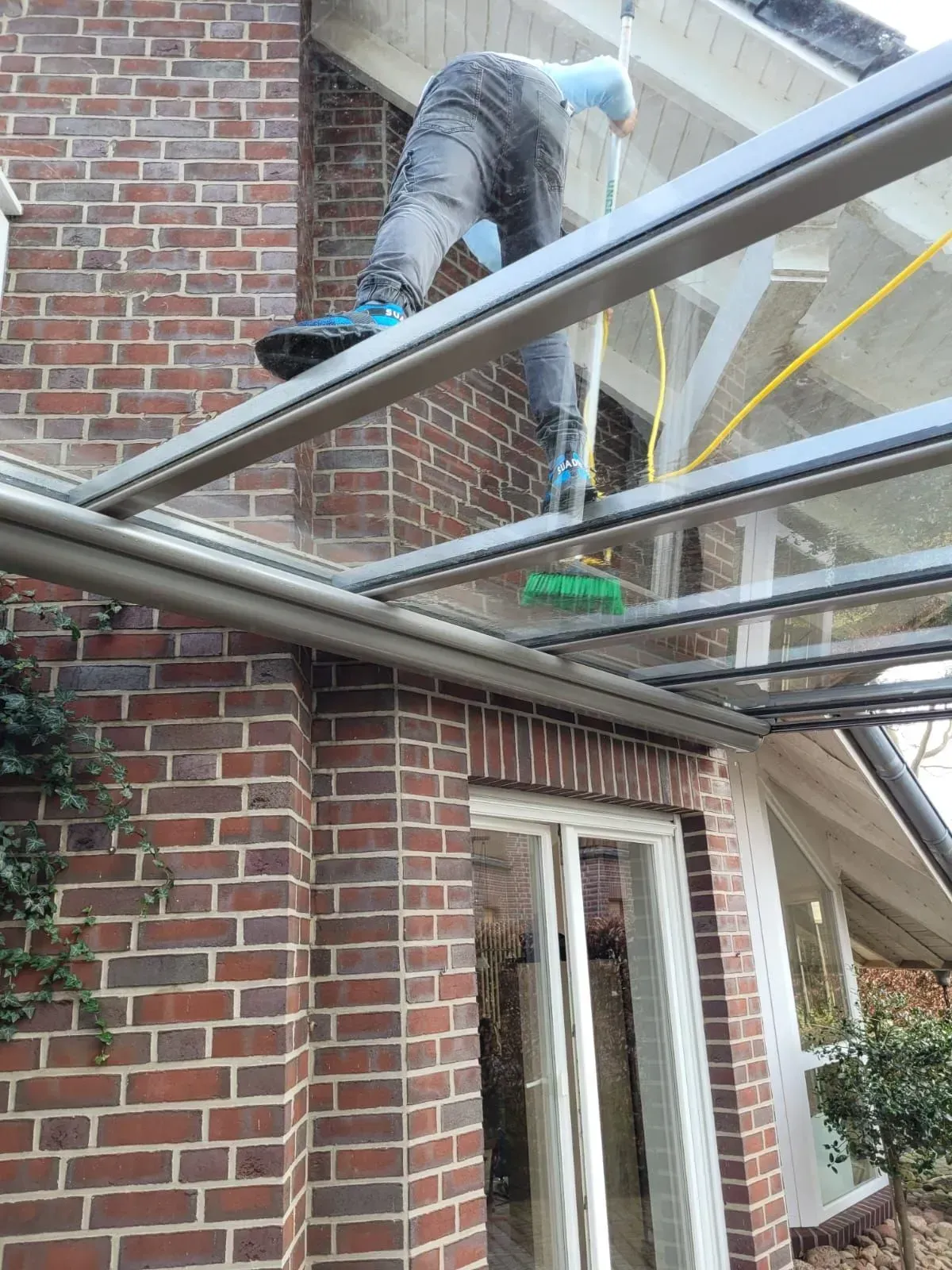 Ein Arbeiter auf einem Dach neben einem Backsteinhaus, mit einer Leiter und einem Metallgerüst.