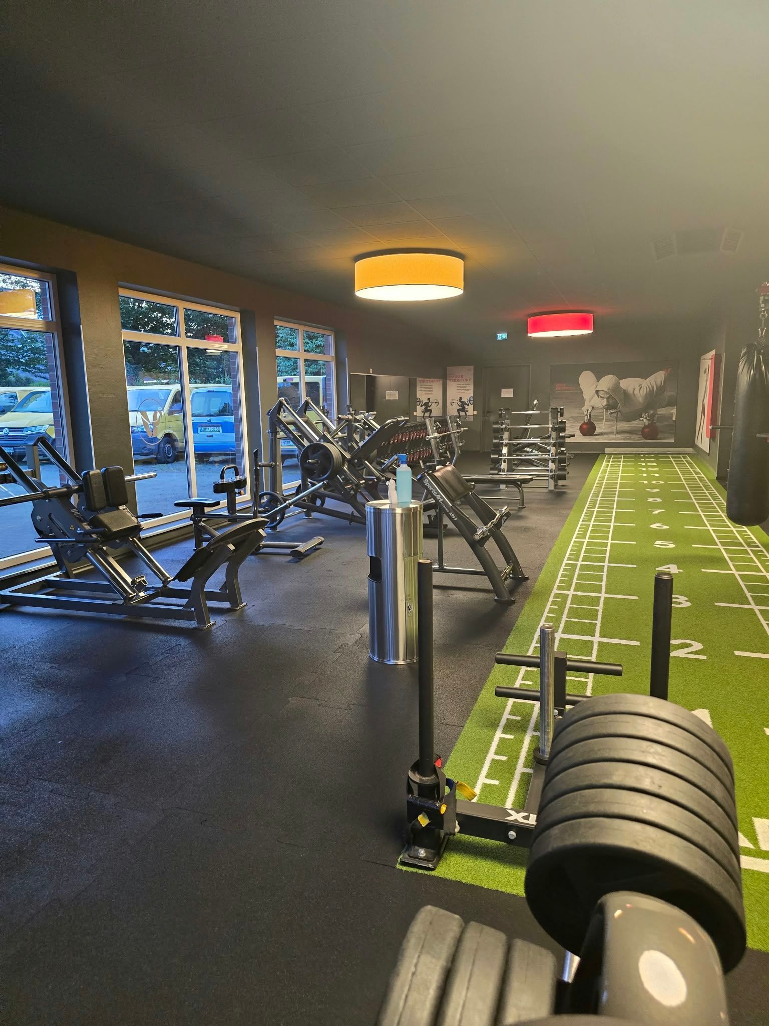 Indoor-Fitnessstudio mit Kraftgeräten, Kunstrasenbahn und Schlittenausrüstung unter warmem Deckenlicht
