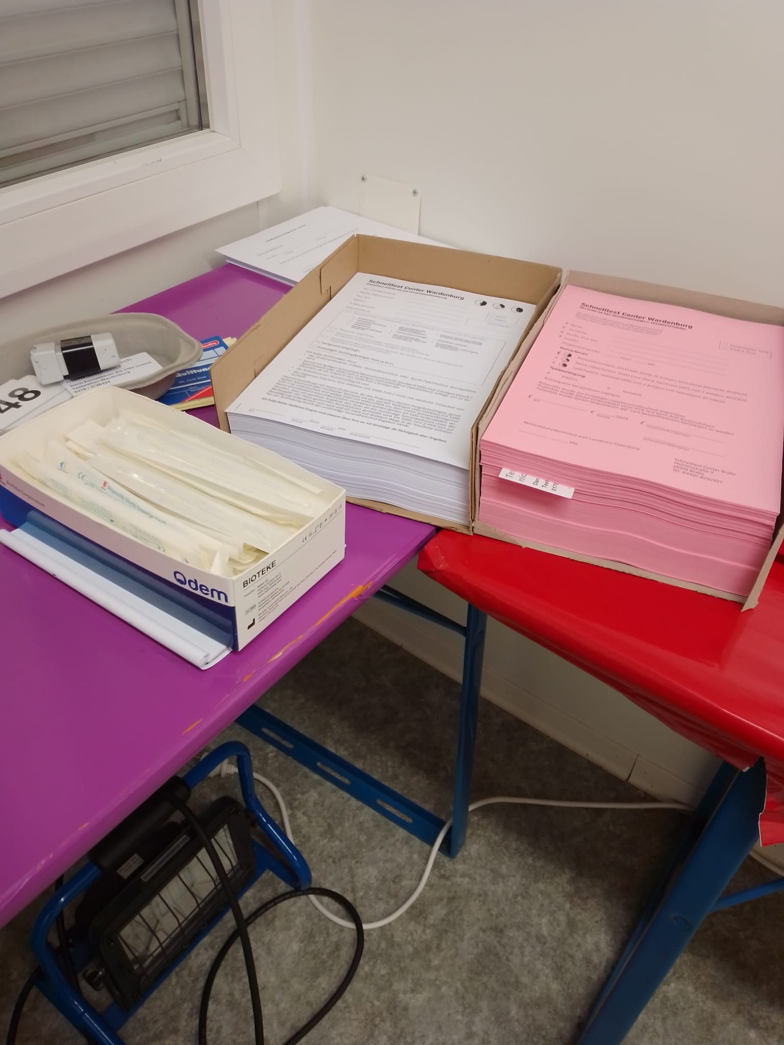 Stapel aus Papieren und Notizbüchern auf violetten und roten Tischen in einem kleinen Raum.