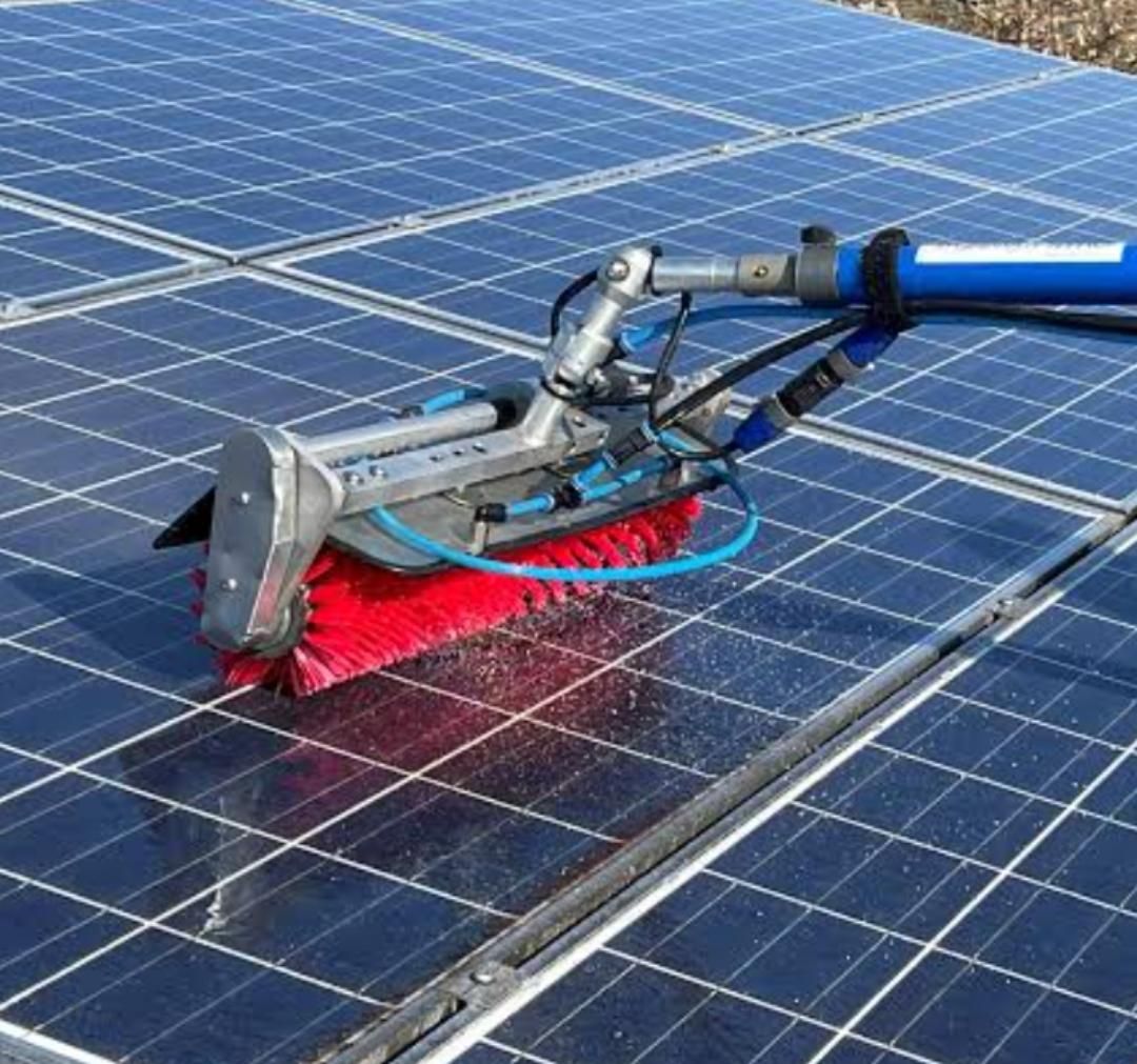 Reinigungsbürste für Solarmodule auf einer blauen Solaranlage, mit roten Borsten und angeschlossenem Schlauch.