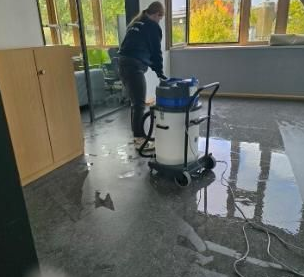 Eine Person wischt drinnen neben einer Reinigungsmaschine und Schränken einen nassen Boden.