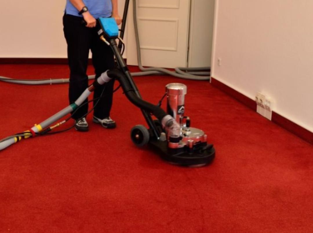 Eine Person bedient eine Einscheibenmaschine auf einem roten Teppich in einem Flur