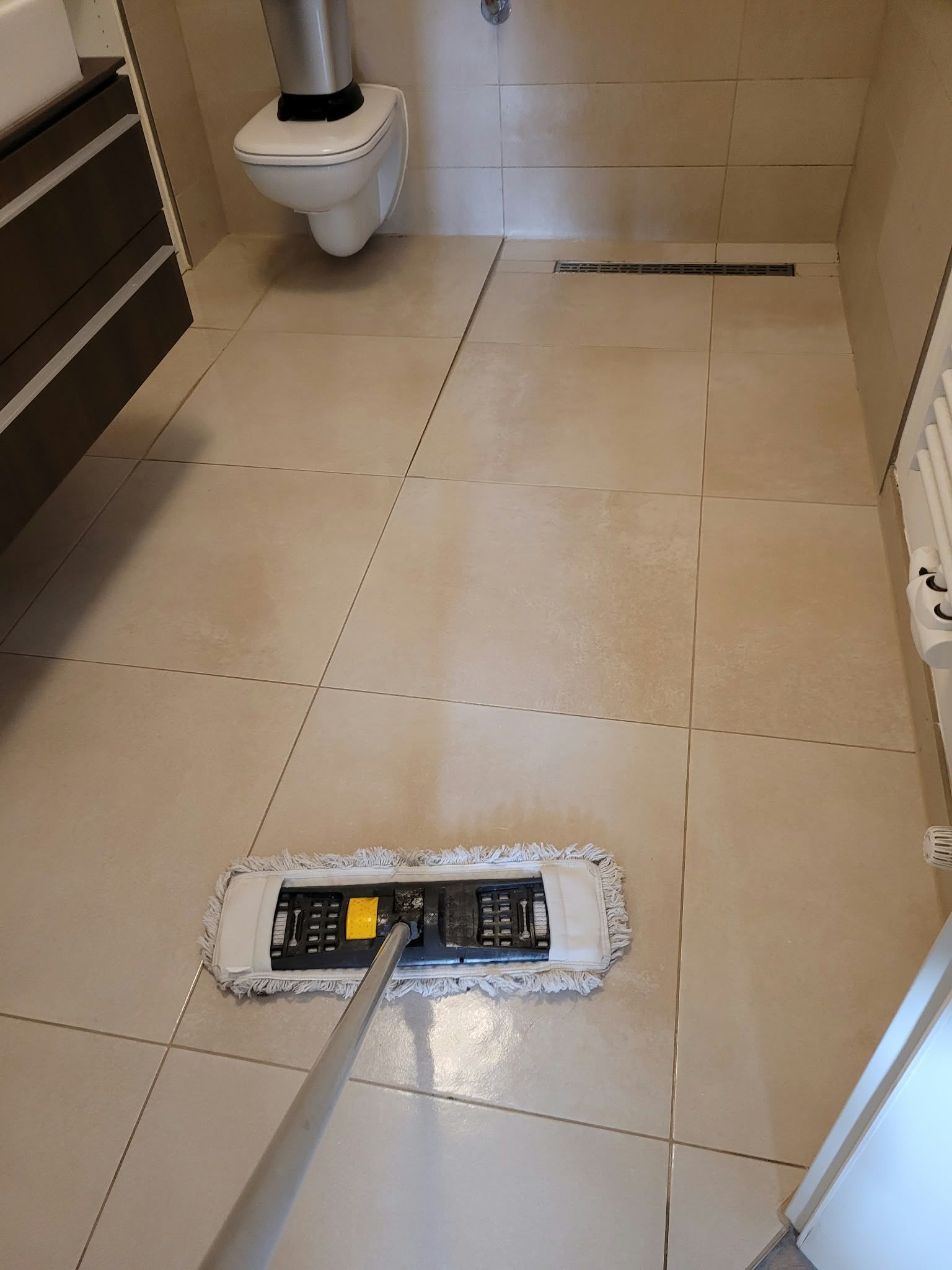 Badezimmerboden wird in der Nähe einer Toilette und eines Bodenablaufs mit einem Mopp gereinigt.