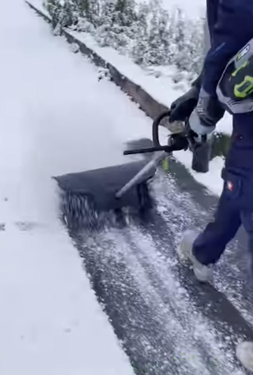 Eine Person schaufelt Schnee von einem Gehweg und räumt einen schmalen Pfad am Rand frei.