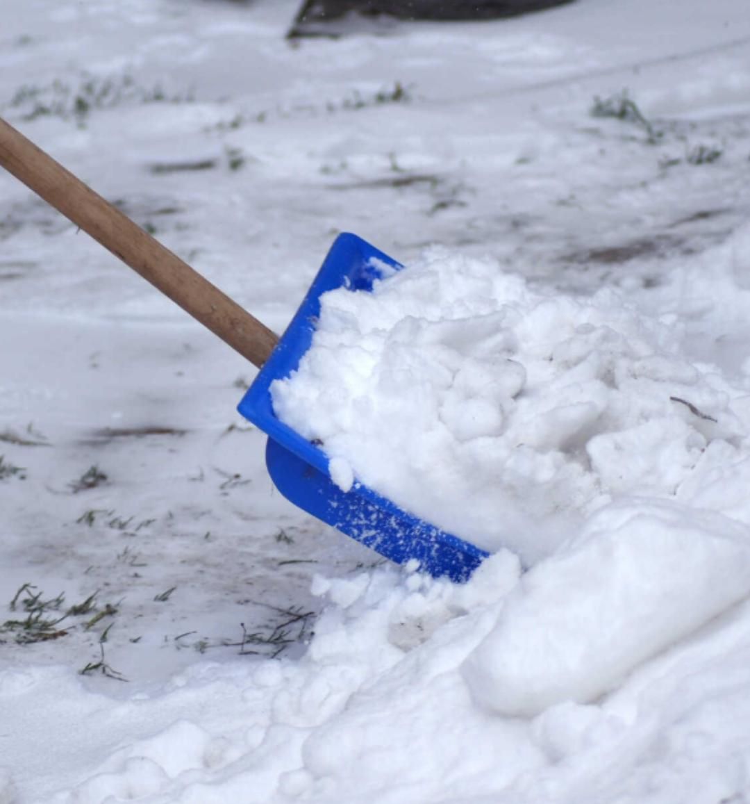 Blaue Schneeschaufel, die Schnee über einen verschneiten Boden schiebt