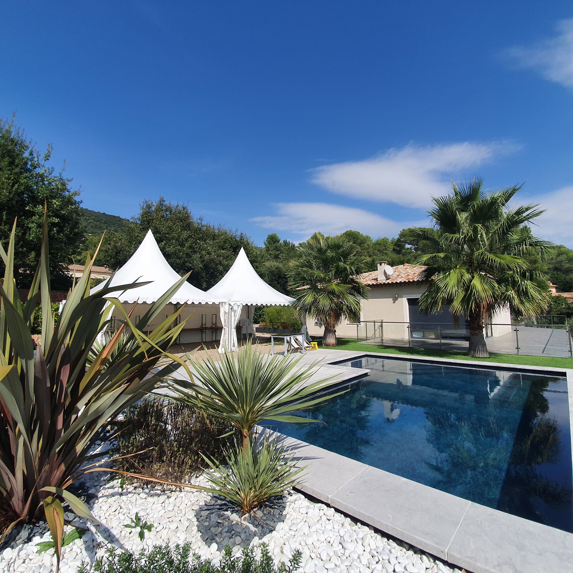 Jardin moderne avec piscine, tentes blanches, palmiers et ciel dégagé