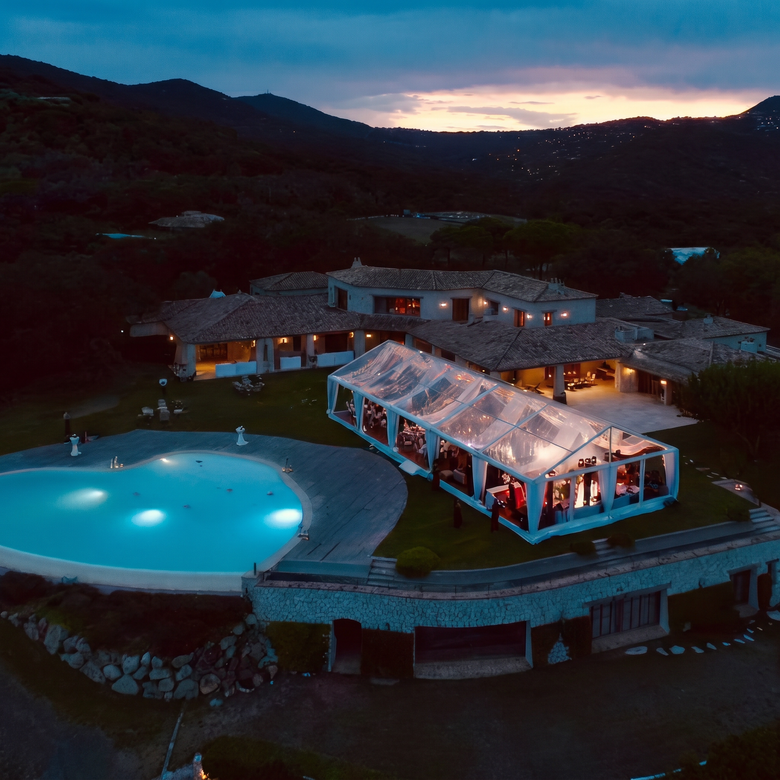 Vue aérienne d'un complexe illuminé, avec une piscine et une tente blanche