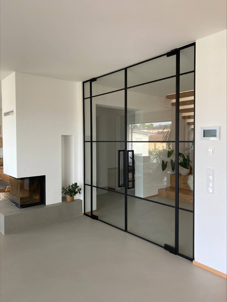 Modernes Interieur mit schwarz gerahmter Glaswand und -tür, weißen Wänden und hellgrauem Boden.