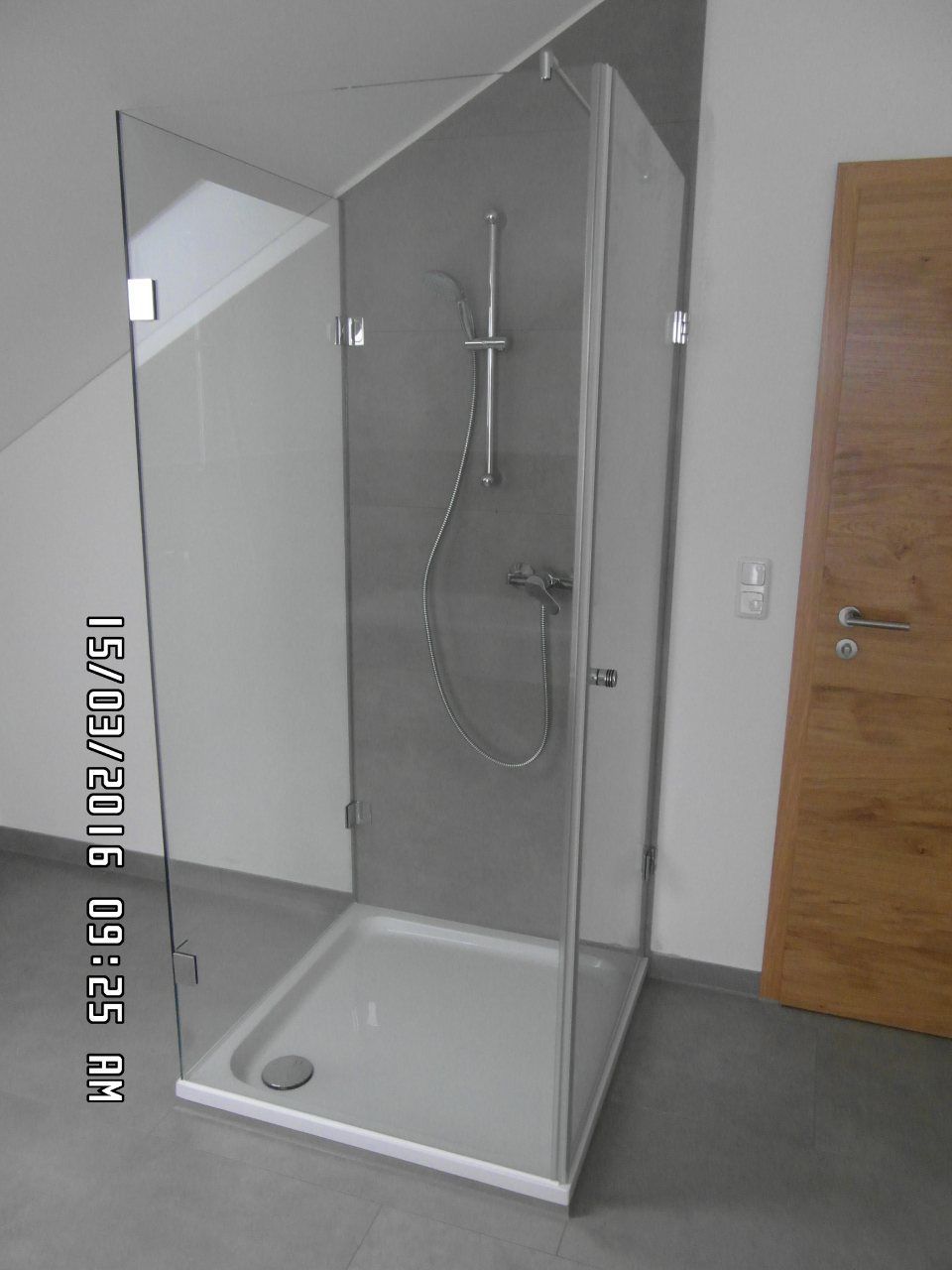 Barrierefreie Duschkabine mit Glastüren, Handbrause und niedrigem Einstieg in einem Badezimmer.