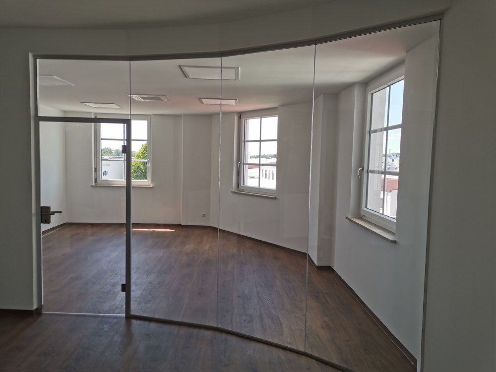 Leerer Büroraum mit gebogenem Glas, Holzboden und großen Fenstern