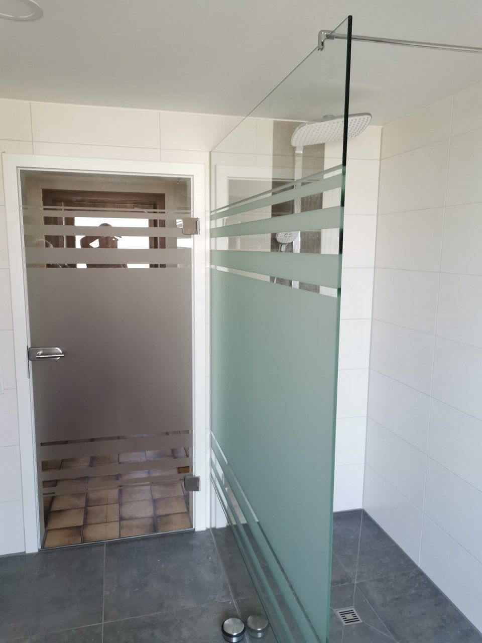 Toiletteneingang mit Milchglas-Kabinentüren und Fliesenboden, vom Flur aus sichtbar