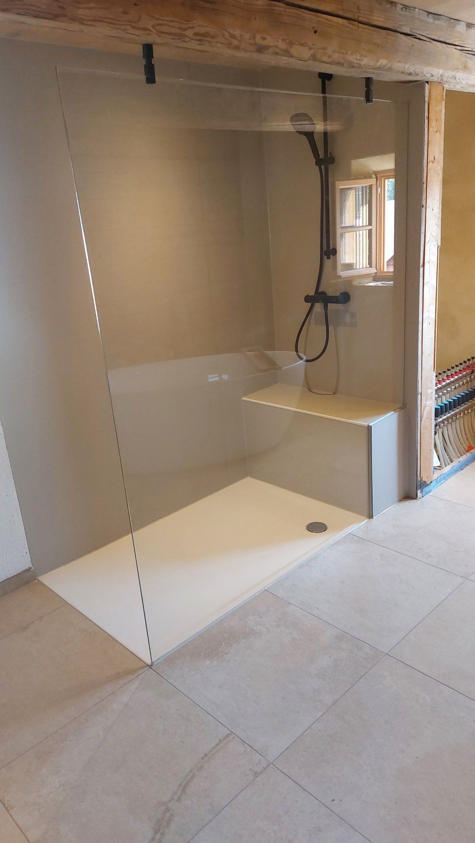 Barrierefreie Duschkabine mit teilweiser Glaswand, weißer Sitzbank und Handbrause in einem im Bau befindlichen Badezimmer