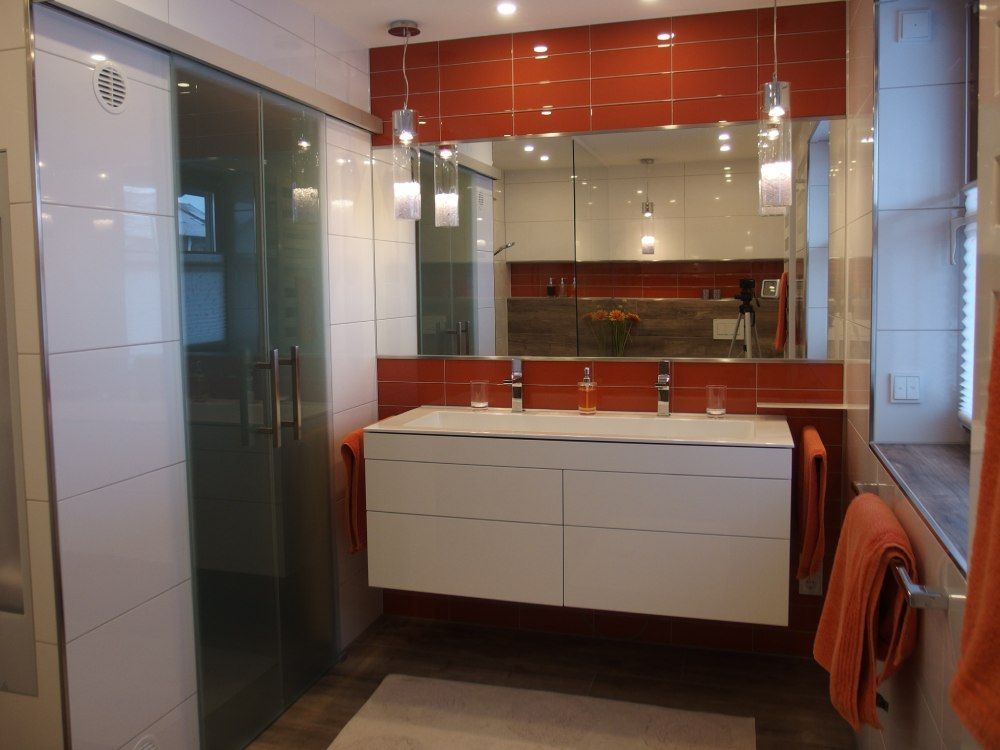 Modernes Badezimmer mit Glasdusche, weißem Waschtisch, roten Fliesenakzenten und einem Wandspiegel