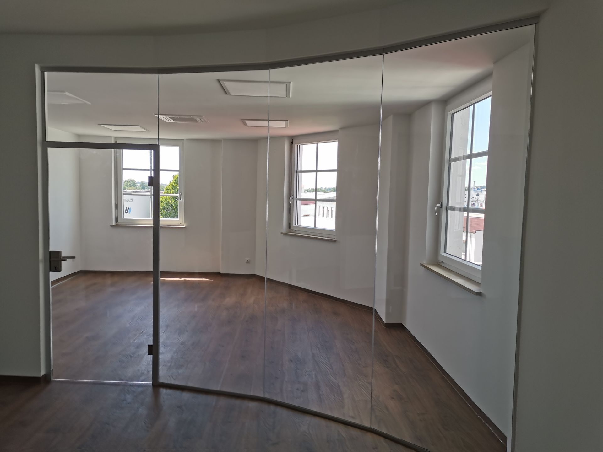 Leeres, modernes Büro mit gebogenen Glaswänden, dunklem Holzboden und großen Fenstern.