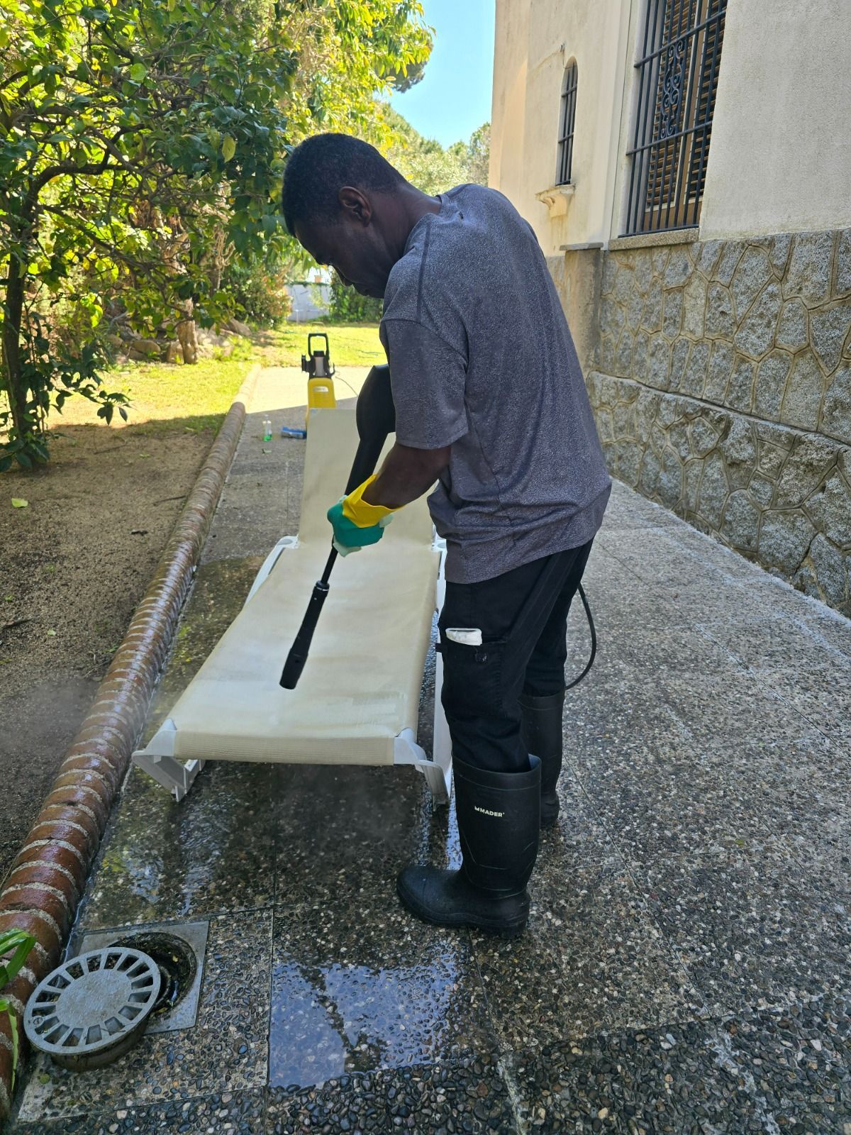 Persona que utiliza una hidrolavadora sobre una superficie exterior; usa guantes y botas.