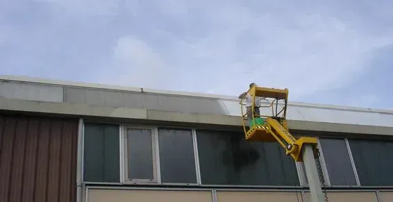 Professionnel sur un élévateur appliquant une laque sur le haut d'un bâtiment