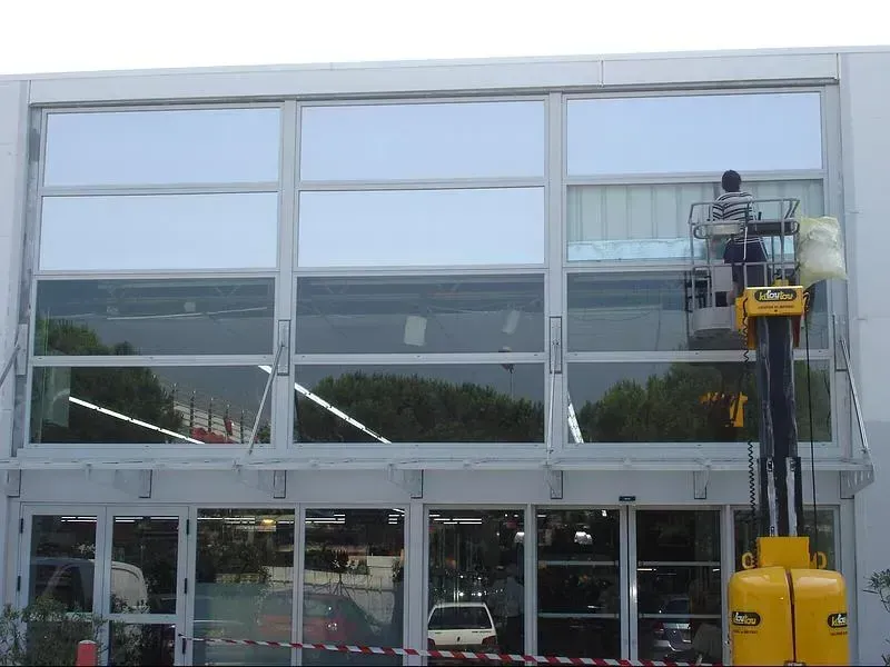 Professionnel sur un élévateur qui applique un film sur les vitres d'une façade