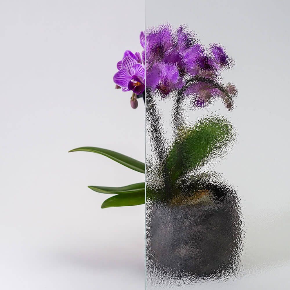 Orchidee im Topf, halb durch strukturiertes Glas sichtbar. Lila Blüten, grüne Blätter.