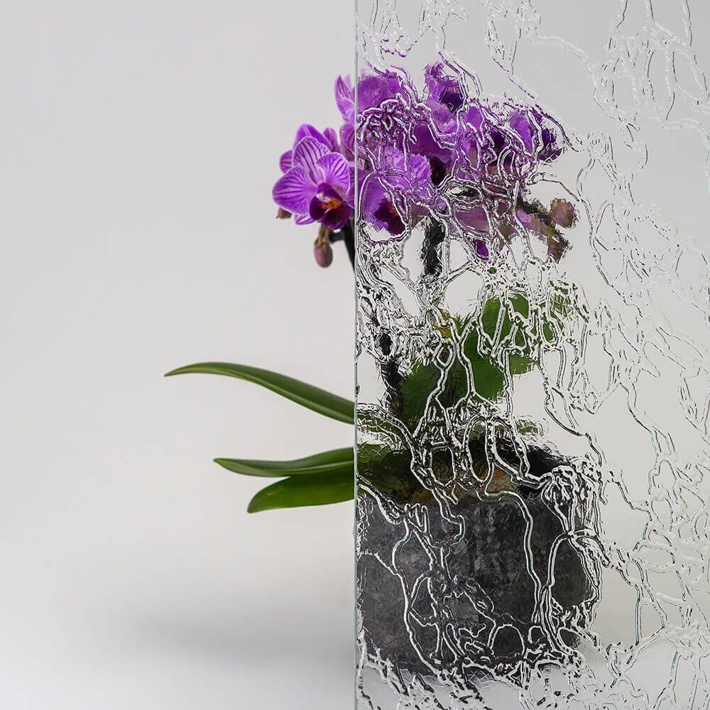 Strukturierte Glasscheibe vor einer lila Orchidee im Topf.